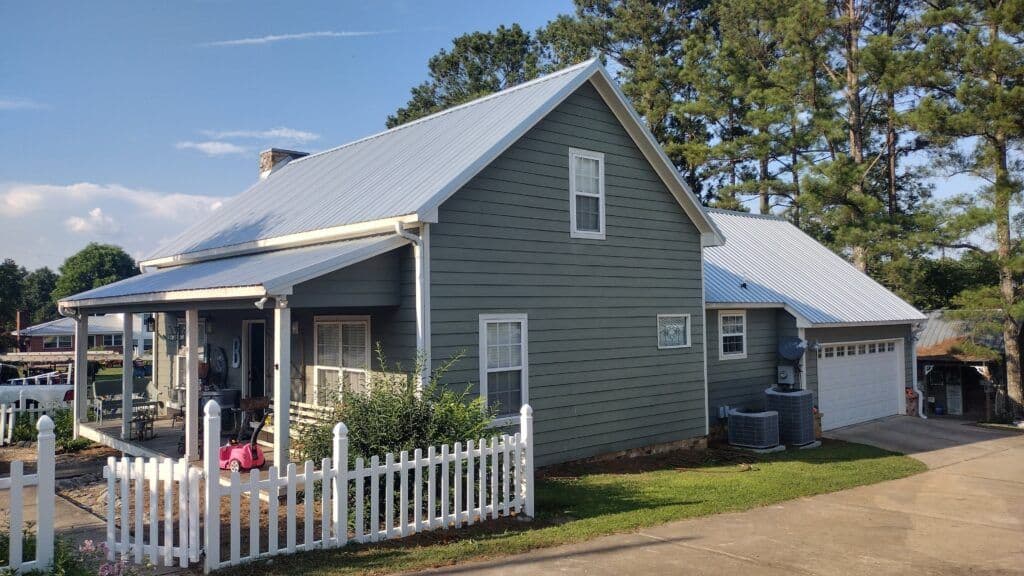 Gray house with a metal roof, white picket fence, and landscaped yard in a suburban setting.