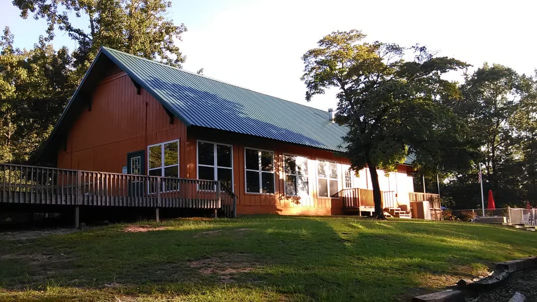 Rustic orange lodge with a blue metal roof surrounded by trees and grass. Ideal for retreats.