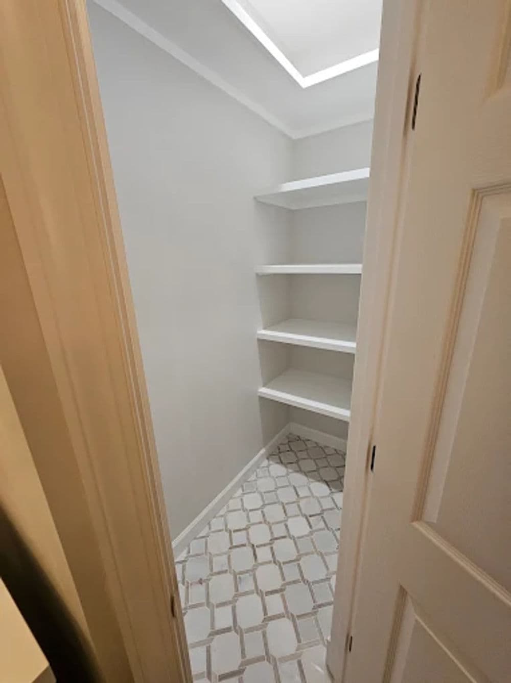 Empty pantry with white shelves and tiled floor, illuminated by natural light.