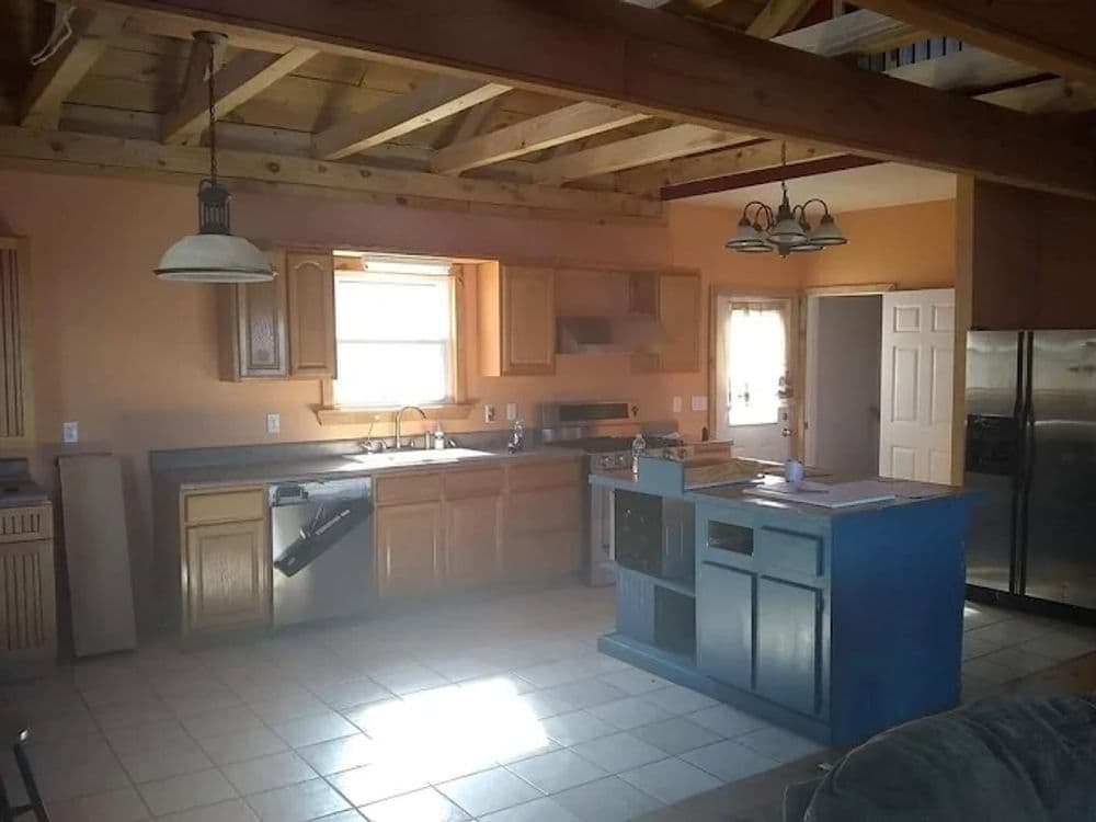 Spacious kitchen with wooden beams, light wood cabinets, and a blue island countertop.