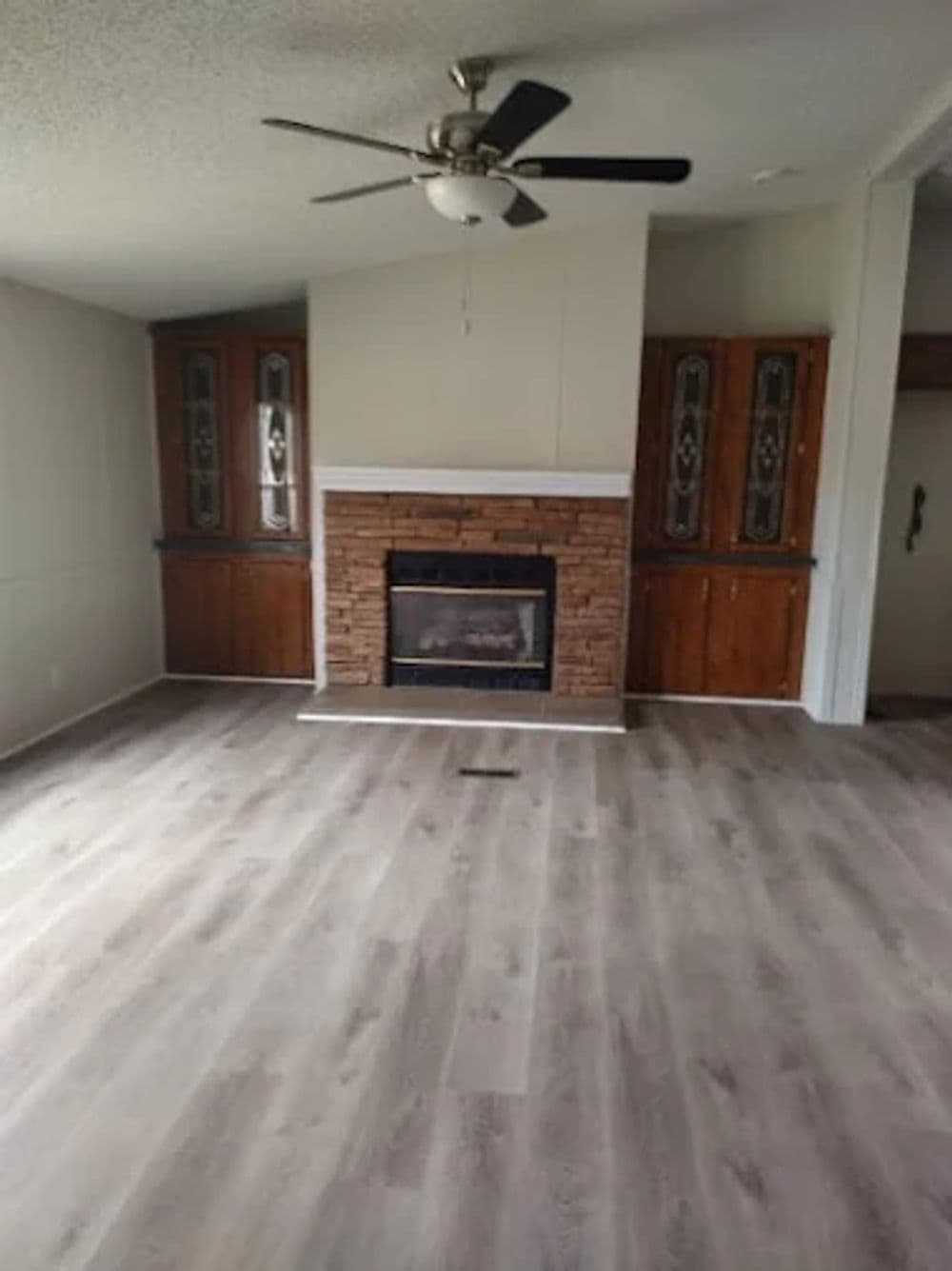 Spacious living room with a fireplace, ceiling fan, and wooden cabinetry. Bright and inviting space.