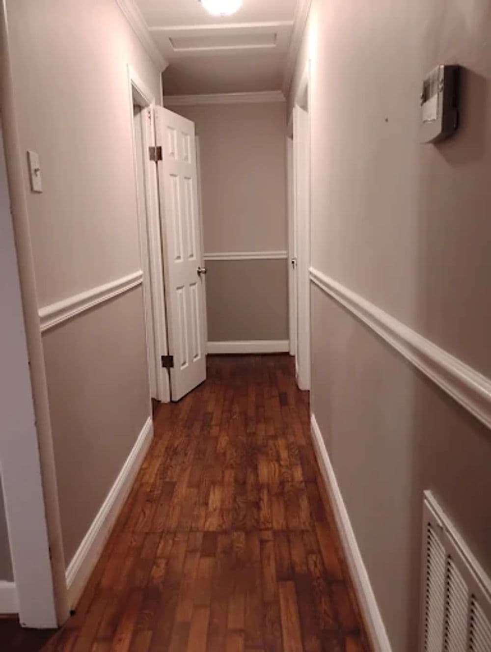 Long hallway with wooden floor, white doors, and light gray walls.