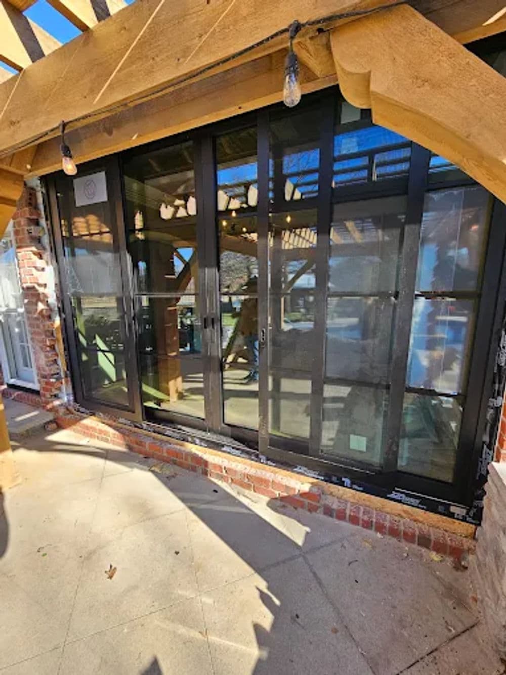 Modern black sliding glass doors in a rustic wood patio setting with string lights.