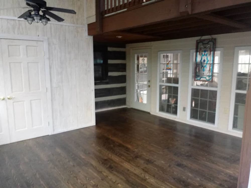 Empty rustic living room with hardwood floors, white walls, and large windows.