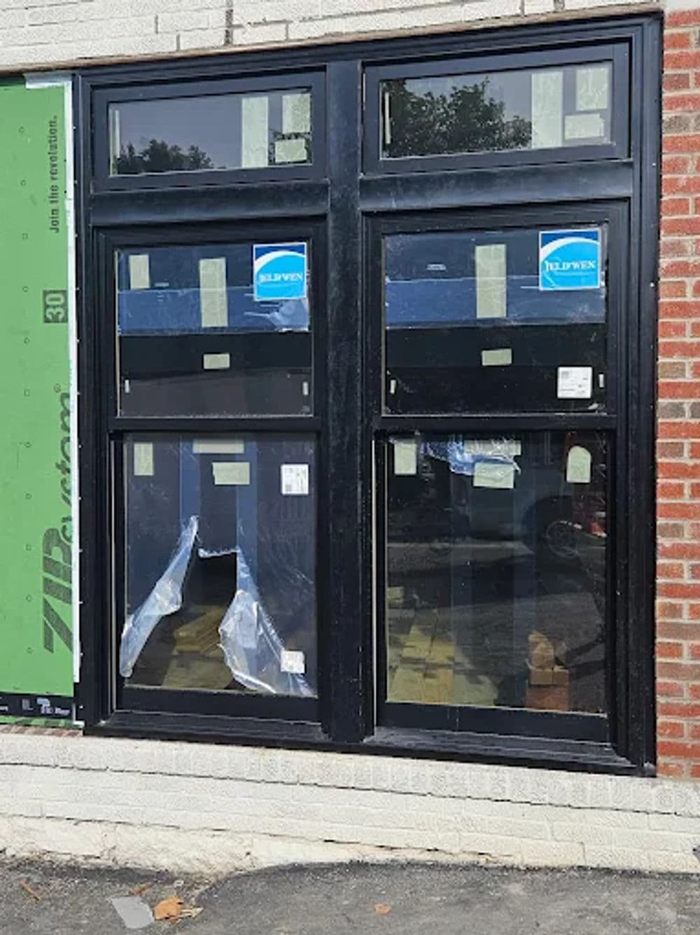 Black window frame with blue stickers in a brick wall, partially covered, under construction.
