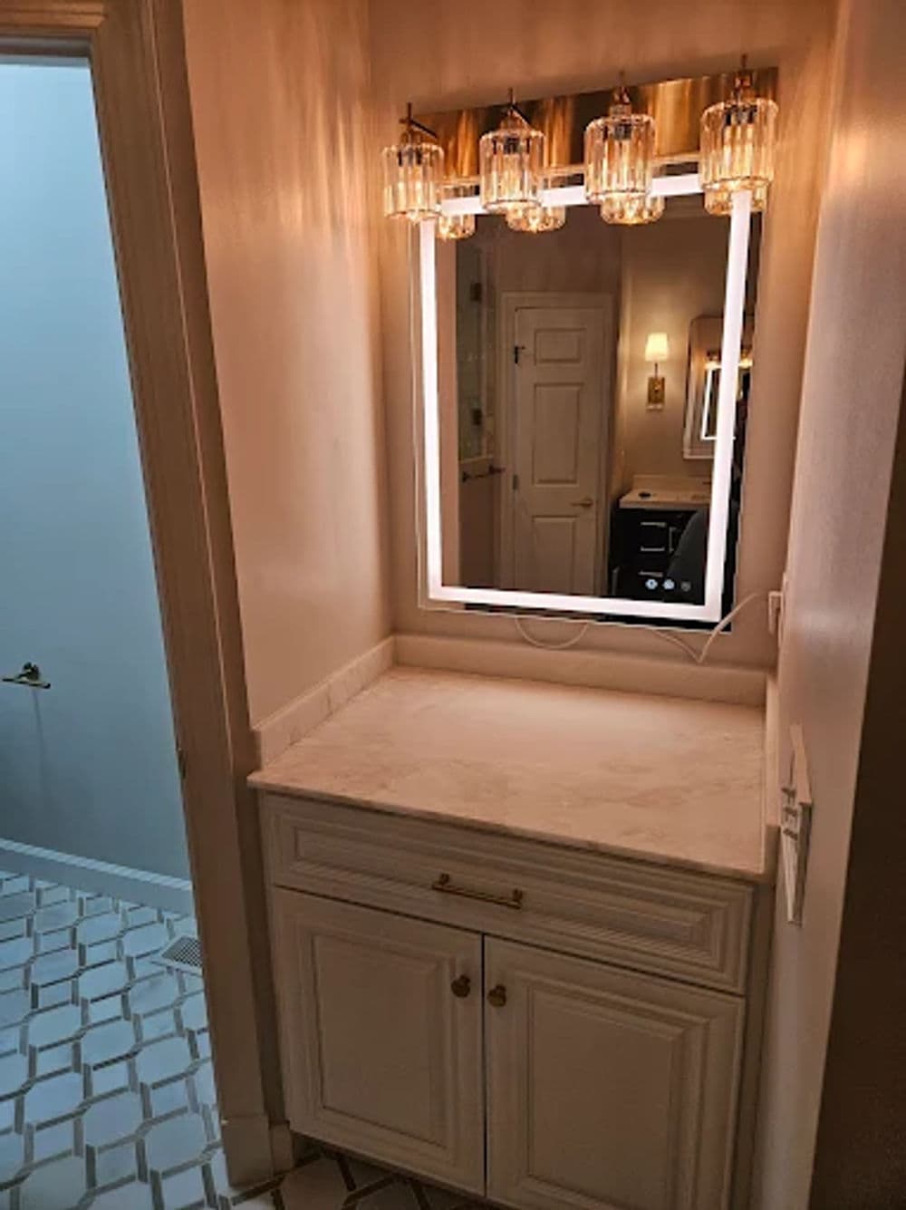Modern bathroom vanity with illuminated mirror and elegant light fixtures. White cabinetry.