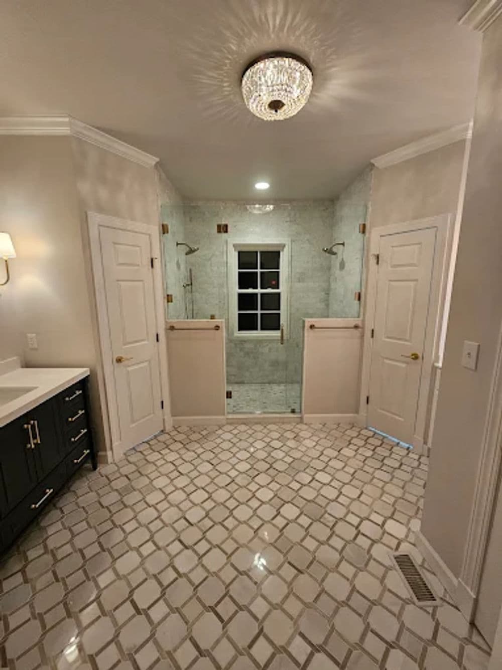 Luxurious bathroom with two glass shower stalls, elegant chandelier, and patterned tile flooring.