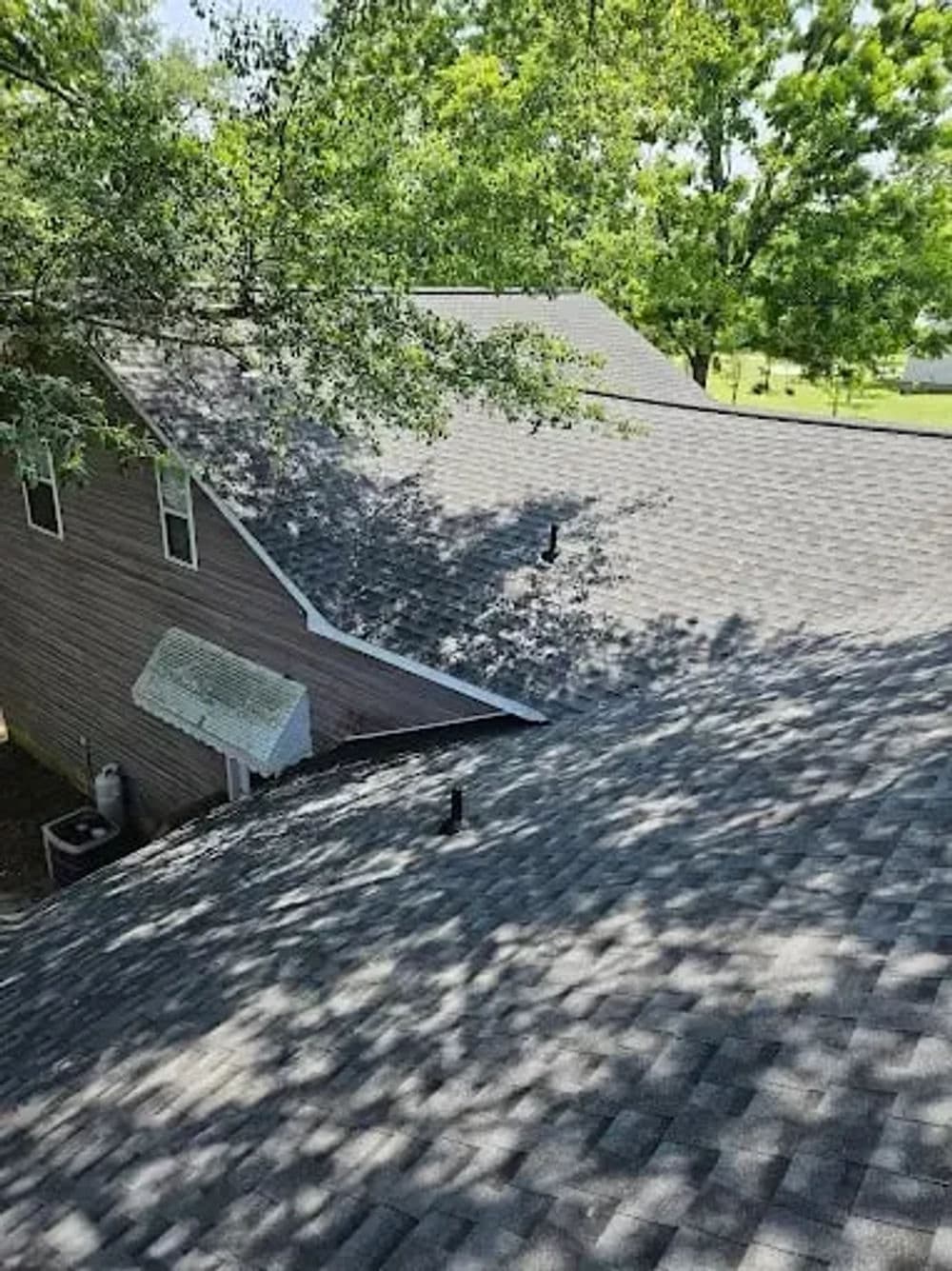 Aerial view of a residential roof with gray shingles and surrounding trees.