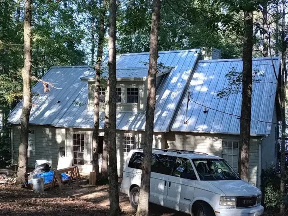 White metal roofed house nestled in wooded area with a van parked in front.