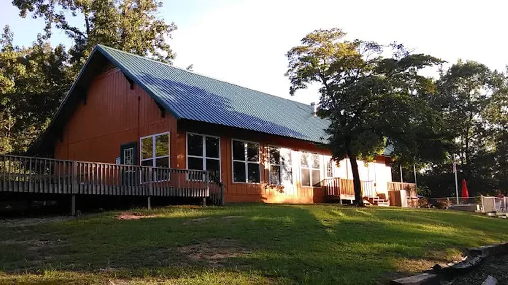 Rustic orange cabin with blue roof surrounded by greenery and wooden deck. Ideal nature getaway.