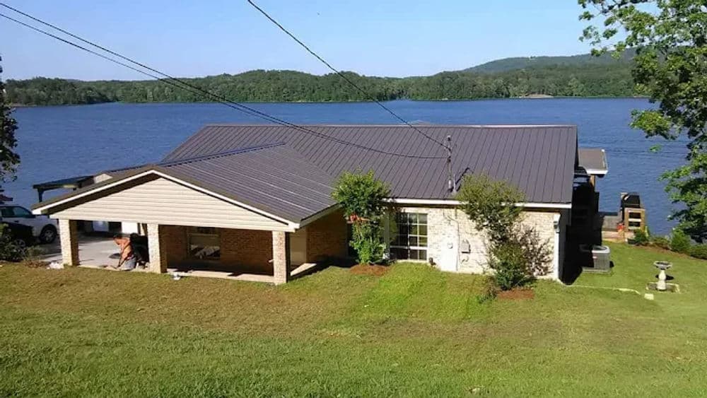 Modern lakeside home with a metal roof, surrounded by greenery and water views.