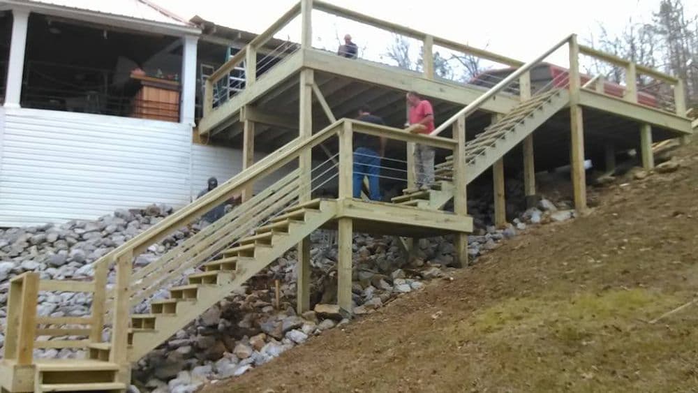 Wooden outdoor staircase leading to a deck, surrounded by rocky terrain and trees.