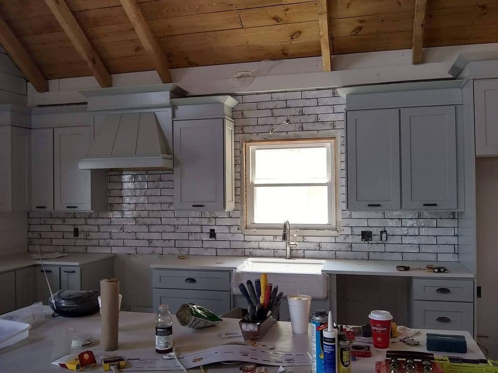 Modern kitchen with gray cabinets, white brick backsplash, and wooden ceiling. Renovation in progress.