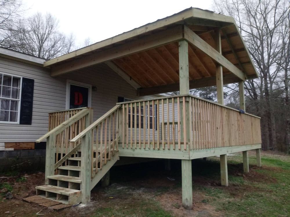 New wooden deck with stairs and railings beside a house in a wooded area.