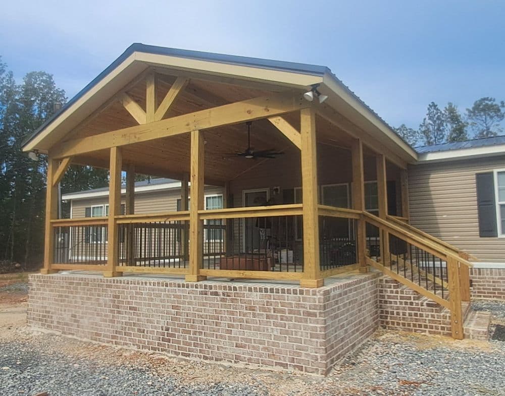 Newly built porch with wooden beams and brick foundation on a modern house exterior.