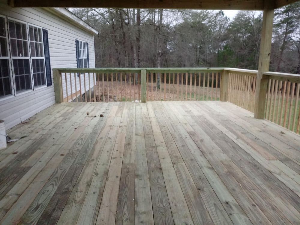 Wooden deck with railing, surrounded by trees, under a covered porch. Ideal outdoor space.