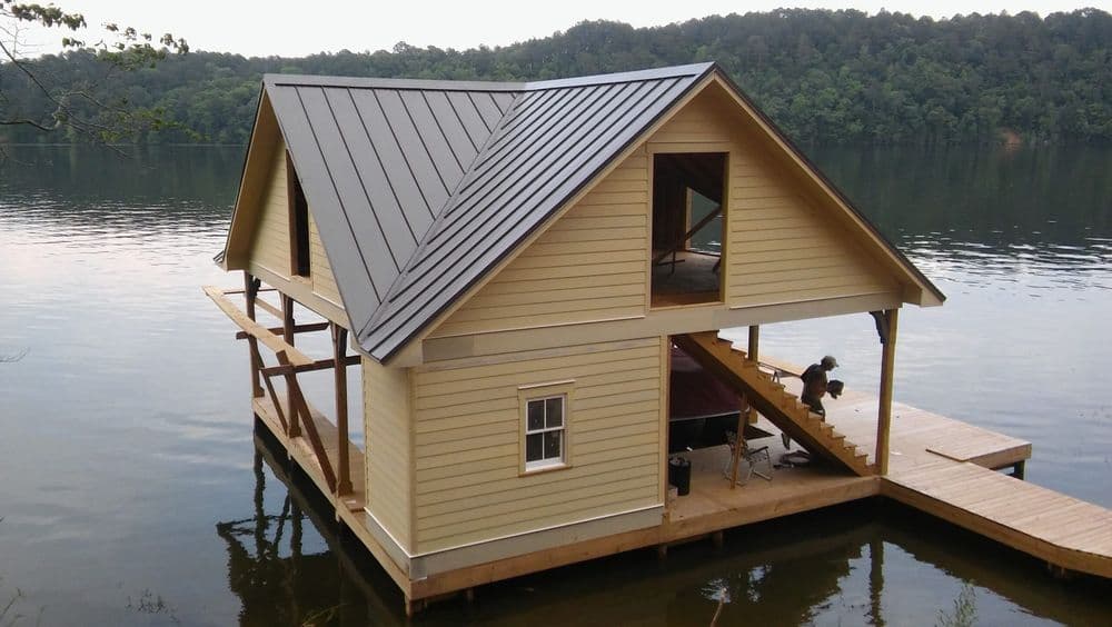 Lakefront house with a metal roof, wooden deck, and construction worker on stairs.