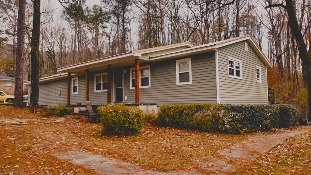 Modern gray house surrounded by trees, with a stone path and seating area in the yard.