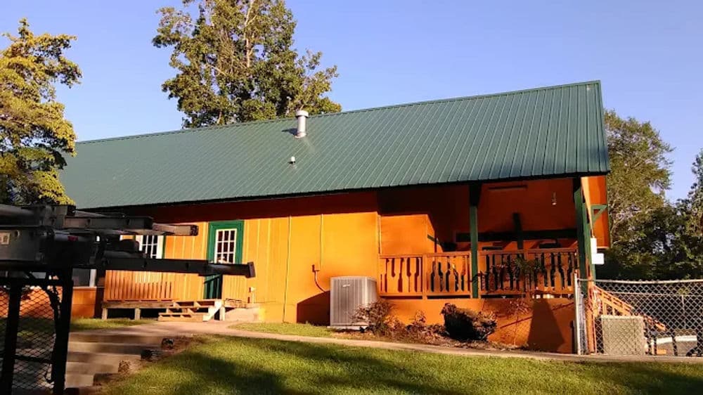 Orange house with green metal roof and porch surrounded by trees and grassy yard.