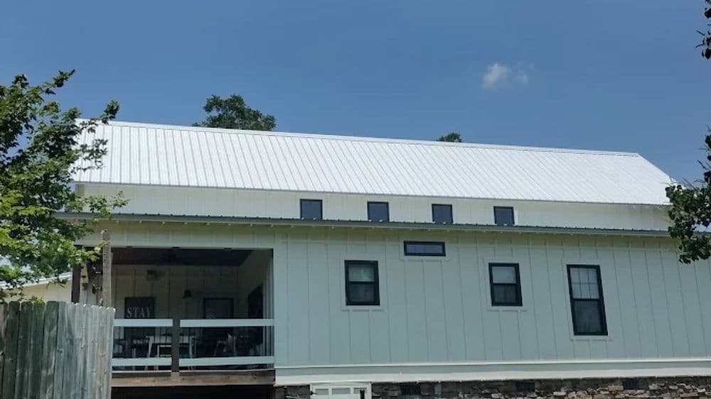 Modern farmhouse with a metal roof and windows, set against a clear blue sky.